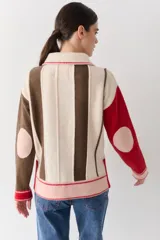 Buzo de punto con cuello polo y cierre frontal de tres botones. Presenta un diseño a rayas verticales en tonos beige y marrón, con mangas en bloques de color rojo y detalles en rosa en los puños y el ruedo.