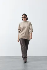 Polera de tejido suave color beige con cuello alto, mangas largas abullonadas con puños elásticos y abertura sutil en la espalda.