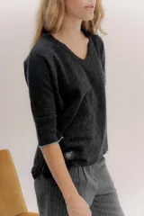 Buzo básico de lambswool color gris oscuro, con escote en V y mangas 3/4. Presenta un fit amplio y tajos laterales. Los puños tienen un detalle de ribete en color celeste y amarillo.