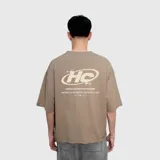 Remera de corte oversize color beige, con estampa gráfica en la espalda que incluye el logo HC y detalles tipográficos en color crema.