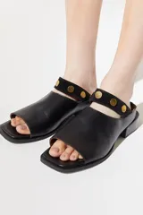 Sandalia de cuero color beige, con diseño slip on y detalle de tachas doradas.