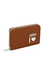 Billetera pequeña con cierre de cremallera, color beige claro, con textura de cuero granulado. Presenta un parche frontal con texto en relieve que dice "TRENDY" y "BE DIFFERENT", y un corazón blanco.