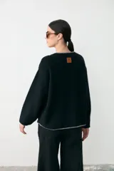Sweater de textura bouclé color negro con detalles de ribete en color gris en el escote en V, puños y bolsillos frontales. Presenta un diseño de manga larga y corte holgado.