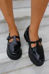 Zapato tipo guillermina en cuero charol color bordó, con suela track negra de goma, cierre con hebilla ajustable y detalle de herrajes metálicos dorados.