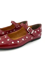 Zapato tipo Mary Jane color cereza charolado, con tachas plateadas, correa con hebilla y suela plana.