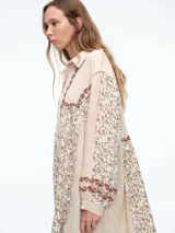 Camisa larga de diseño patchwork con cierre frontal de botones, confeccionada en una combinación de texturas lisas y estampados florales con detalles bordados en el canesú y los puños.