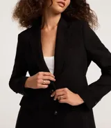 Blazer negro de corte sastrero, con solapas en el cuello, doble botonadura frontal y bolsillos falsos con solapa.