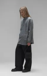 Camisa de manga larga en tejido twill color gris melange, con corte oversize. Presenta cuello clásico, cierre frontal con botones y tres bolsillos delanteros, uno de ellos oculto.