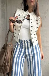 Chaleco estilo militar color natural, con cuello mao, múltiples botones metálicos decorativos en la parte frontal y detalles de flecos en las sisas.