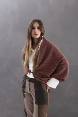 Saco tipo capa de tejido de lanilla con diseño de ochos, color ciruela. Presenta mangas amplias y cierre frontal con alamar de cuero y carey. Incluye detalles de cinta tejida en rayas con tonos nude, ciruela y verde.
