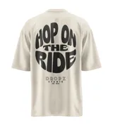 Remera color beige con efecto lavado, de corte relajado y caída amplia. Presenta una estampa tipográfica oversized en la espalda con la frase "Hop On The Ride" en negro y el logo "Dropz Studio Est. 2025" debajo. En el frente, tiene un mini logo de Dropz en el pecho.