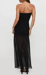 Vestido largo negro de corte sirena, con escote palabra de honor (strapless), diseño ajustado en el torso con detalles drapeados en los laterales y falda larga semitransparente con tajo frontal.