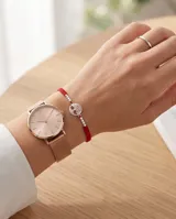Pulsera de hilo rojo con técnica de macramé, que presenta un dije central circular con diseño calado de árbol de la vida en plata y pequeñas esferas plateadas decorativas a ambos lados.