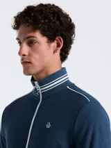 Campera deportiva azul marino de tejido doble con cierre frontal, cuello alto y bolsillos laterales. Presenta rayas blancas en el pecho, hombros y puños, y logo bordado de la marca en el pecho.
