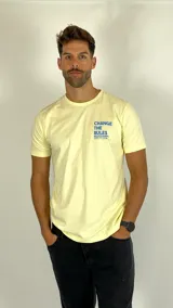 Remera de algodón color amarillo suave, con cuello redondo y mangas cortas. Presenta una estampa frontal pequeña en el pecho con el texto 'CHANGE THE RULES' en color azul.