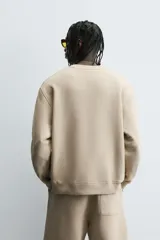 Sudadera de algodón color beige claro, corte relajado, cuello redondo y manga larga. Presenta bordado en relieve en el frente con texto en cursiva de color cobre.