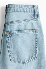 Jean tobillero de cinco bolsillos en denim de algodón rígido, con piernas rectas de corte holgado y cintura de tiro alto con cierre y botón.