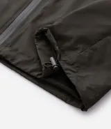 Campera rompevientos color tostado, con capucha ajustable mediante cordones, cierre frontal completo y puños elásticos. Presenta un diseño minimalista y funcional, ideal para protección contra el viento.