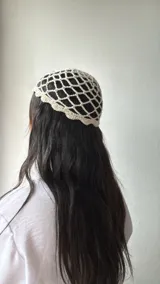 Gorro de crochet color crudo con diseño de red y dije plateado colgando.