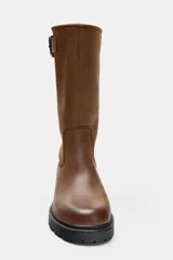 Bota de piel color marrón de caña alta, con detalle de hebilla metálica en la parte superior, efecto desgastado y suela dentada negra.