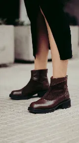 Bota corta de cuero negro con diseño de paneles que combina cuero liso y gamuza. Presenta puntera cuadrada, cierre trasero y suela con plataforma y taco bajo geométrico.