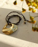 Collar con cordón negro y dije dorado con forma irregular y abertura circular.