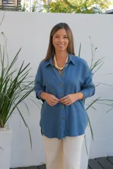 Camisa de jean de corte oversize, con cuello clásico, cierre frontal de botones y mangas largas. Presenta un diseño con bolsillos laterales integrados y ruedo redondeado.