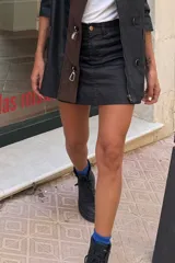 Falda mini de efecto engomado en color negro, con costuras a contratono en color marrón. Presenta diseño de cinco bolsillos, cierre frontal con botón y etiqueta de cuero con logo en la parte posterior.