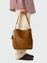 Bolso tipo cubo de gamuza en color marrón, con asa de hombro ajustable y detalle de dije metálico colgante.