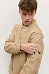 Campera bomber de gabardina color tostado, con cierre frontal y bolsillos laterales, puños y cintura elastizados de rib.