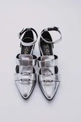 Sandalias plateadas con punta cerrada, tiras entrecruzadas y pulsera al tobillo con hebilla. Taco cuadrado negro.