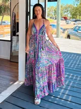 Vestido largo tipo solera, con escote en V y tirantes finos, confeccionado en seda estampada con motivos florales y patrones geométricos en tonos azules, naranjas y morados. Presenta un corte amplio y volados en el ruedo.