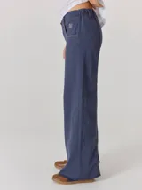 Pantalón de corte relajado color marrón oscuro, con costuras en hilo rojo a contraste y bordado decorativo en el bolsillo delantero.