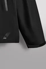 Cazadora deportiva color marrón confeccionada en tejido técnico de tres capas con membrana impermeable. Cuenta con cuello alto con capucha ajustable, mangas largas con puños reforzados ajustables, aberturas con cremallera en axilas, bolsillos frontales con cremallera y bajo ajustable con elásticos laterales.