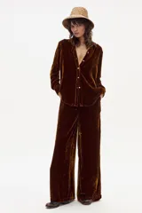 Pantalón de terciopelo color marrón oscuro con textura brillante y pierna ancha. Presenta tiro medio-alto con elástico en la espalda y corte limpio en el delantero.