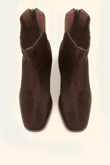 Bota de caña media confeccionada en cuero vacuno negro, con diseño minimalista y cierre trasero. Presenta un taco cilíndrico de madera tallada y punta cuadrada.