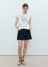Remera de manga corta color blanco con cuello redondo y diseño recto. Presenta un estampado frontal en tonos azules con ilustraciones de caracoles y la inscripción "Les Coquillages".