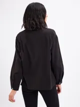 Camisa blanca de algodón, de manga larga, con detalle de tiras cruzadas en el canesú delantero y cierre frontal con botones.