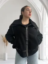 Campera negra de corderito con cuello solapa, cierre frontal con cremallera metálica y detalles de cuero sintético en cuello, solapa, cierre y bolsillos.