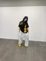 Remera negra de corte regular con estampado gráfico en color amarillo. Presenta inscripciones con estética oriental en la parte superior izquierda y en el lateral derecho. Confeccionada en algodón de alto gramaje con cuello reforzado y grifa de la marca en la manga.