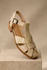 Sandalias de cuero color cobre metalizado, tipo franciscanas, con diseño de tiras cruzadas, puntera cerrada y tira ajustable con hebilla en el tobillo. Cuentan con un pequeño tacón plano.