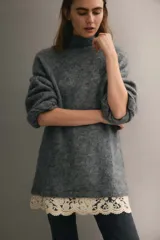 Buzo de punto holgado con mezcla de lana y mohair, color gris. Presenta cuello alto, hombros caídos y mangas largas. El bajo está decorado con un ribete de encaje en color crema en contraste.