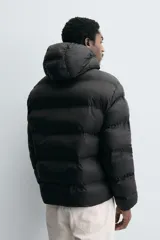Campera puffer negra con capucha ajustable con elásticos, cuello alto, cierre frontal con cremallera, bolsillos laterales y puños elásticos ajustables.
