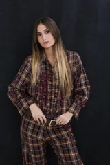Camisa de manga larga con estampado de cuadros escoceses en tonos marrones, negros y beige. Presenta volados verticales en la pechera, botones metálicos en tono oro viejo y puños con detalles de volados.
