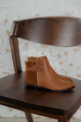 Botas cortas de cuero negro con paneles traseros de gamuza, cierre lateral y detalle de correa con hebilla metálica en el tobillo.