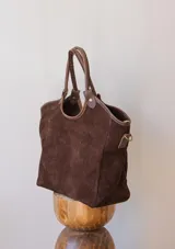 Cartera tipo tote de gamuza negra, con doble asa de mano y correa larga ajustable y desmontable. Cuenta con un diseño estructurado y base plana.