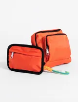 Bolso bandolera pequeño color beige, confeccionado en poliéster con cierre frontal y compartimento principal. Incluye un llavero decorativo de cuerda multicolor con mosquetón.