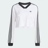 Blusa cropped de manga larga Adidas Adicolor en color blanco, con cuello en V y puños acanalados en negro. Presenta las tres tiras clásicas de la marca en color negro a lo largo de las mangas y el logo del trifolio bordado en el pecho.