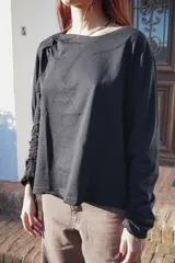 Remera negra de mangas largas con detalle de frunce en una manga y drapeado en el hombro.