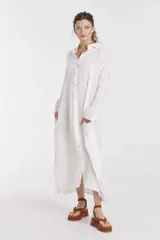 Vestido camisero largo de lino color blanco, con cuello clásico, mangas largas, cierre frontal con botones y bolsillos laterales.